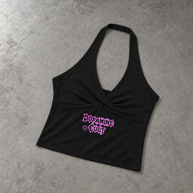A black halter crop top with a twisted front detail and a pink 'DARKLINE CULT' graphic, laid flat on a textured gray concrete surface.